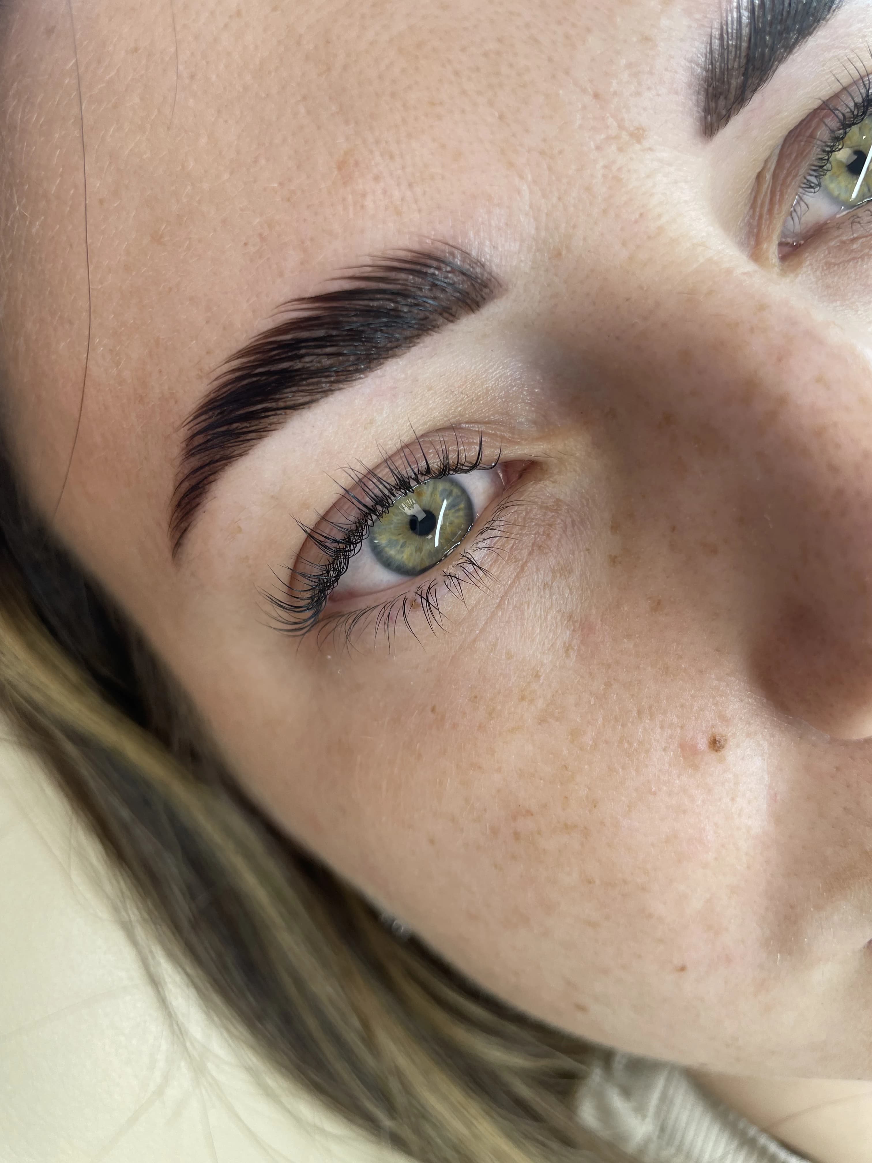 Feathered laminated brow brushed upward with tinted curled lashes on green eyes at My Beauty Space.