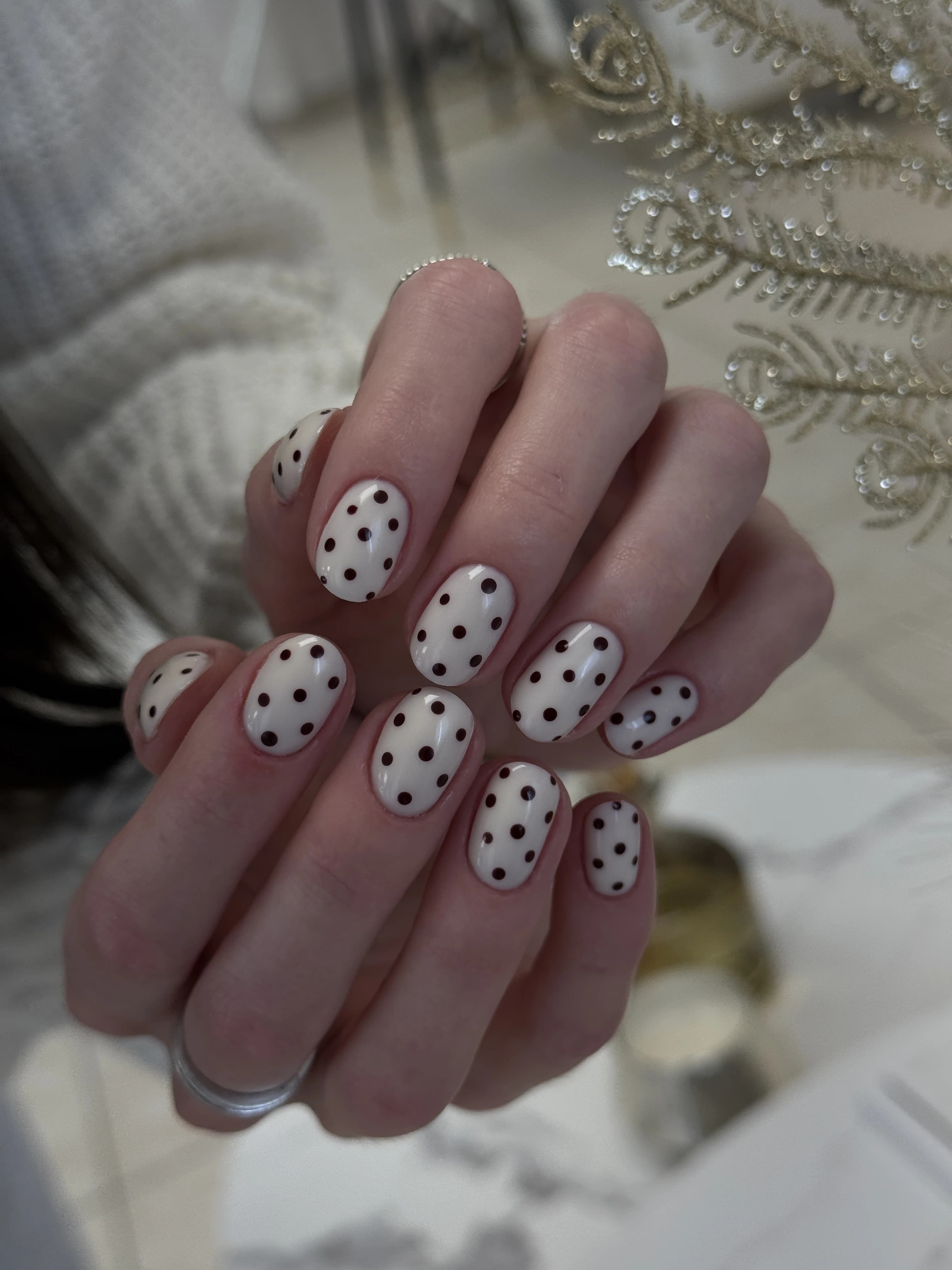 Mississauga nail art with dark polka dots on creamy off-white oval nails, fingers interlaced in a white sweater.