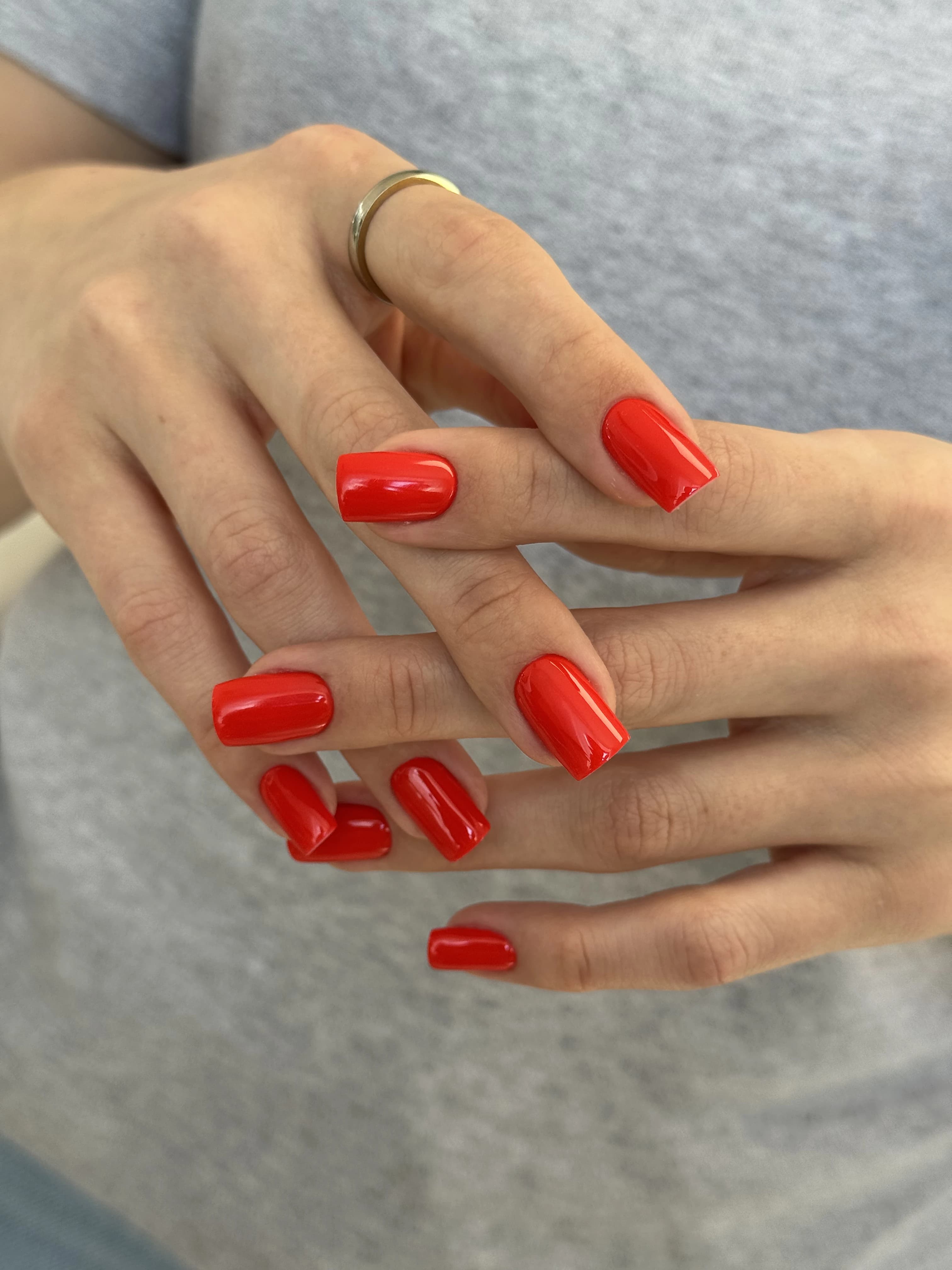Glossy cherry-red gel polish on medium squoval nails with a gold band ring, a bold look from My Beauty Space Mississauga.