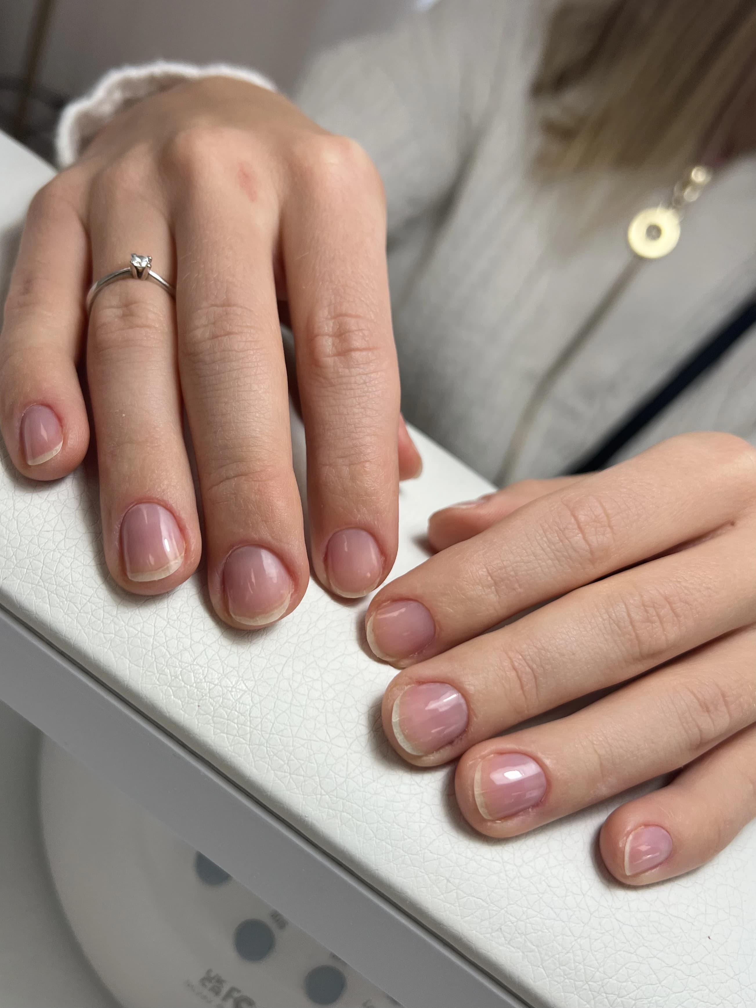 Mississauga Japanese manicure with short rounded nails in a sheer pink nude gloss, resting on a white salon armrest.