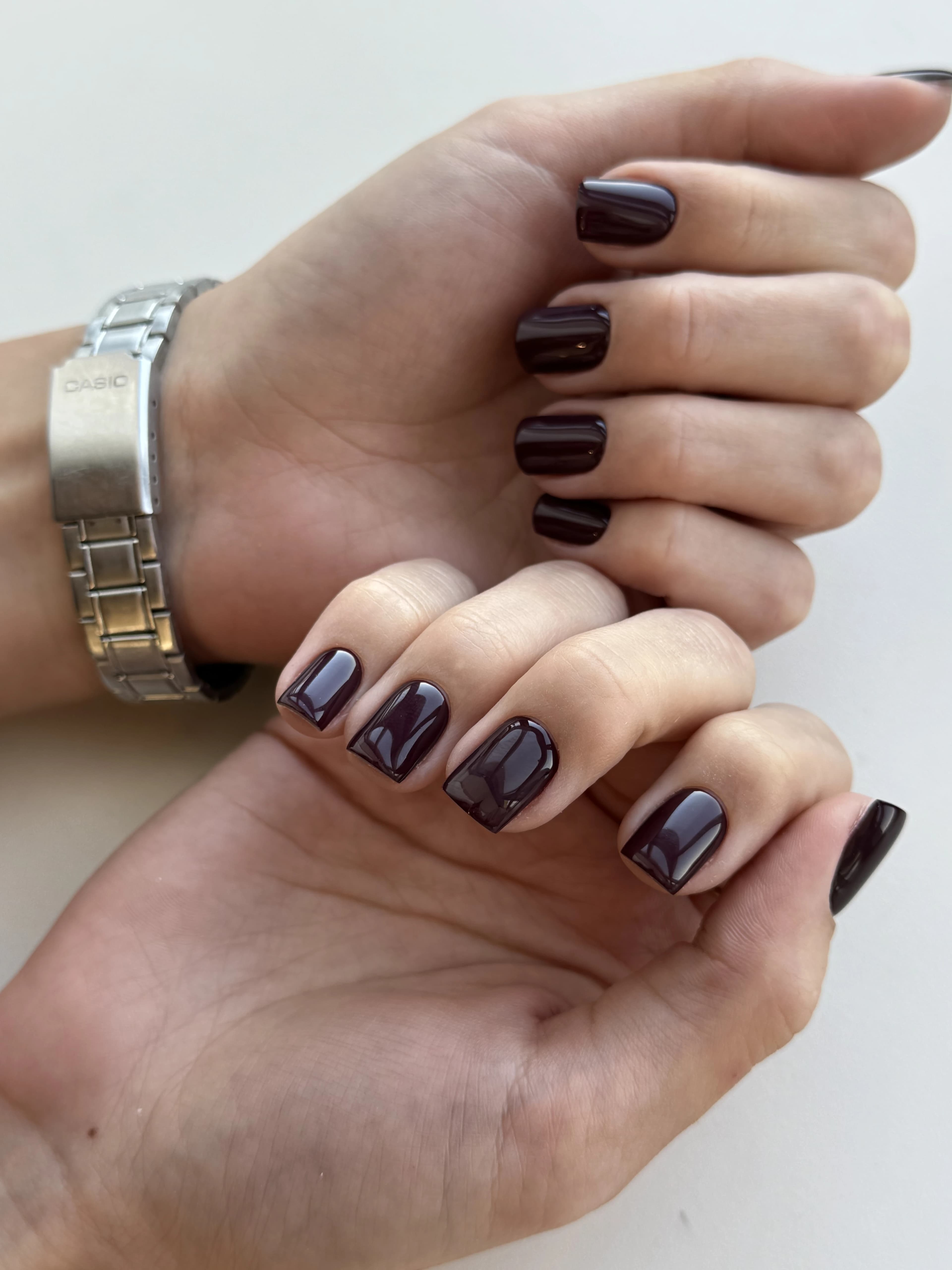Dark plum hard gel on short square nails beside a silver Casio watch, a rich finish from My Beauty Space Mississauga.