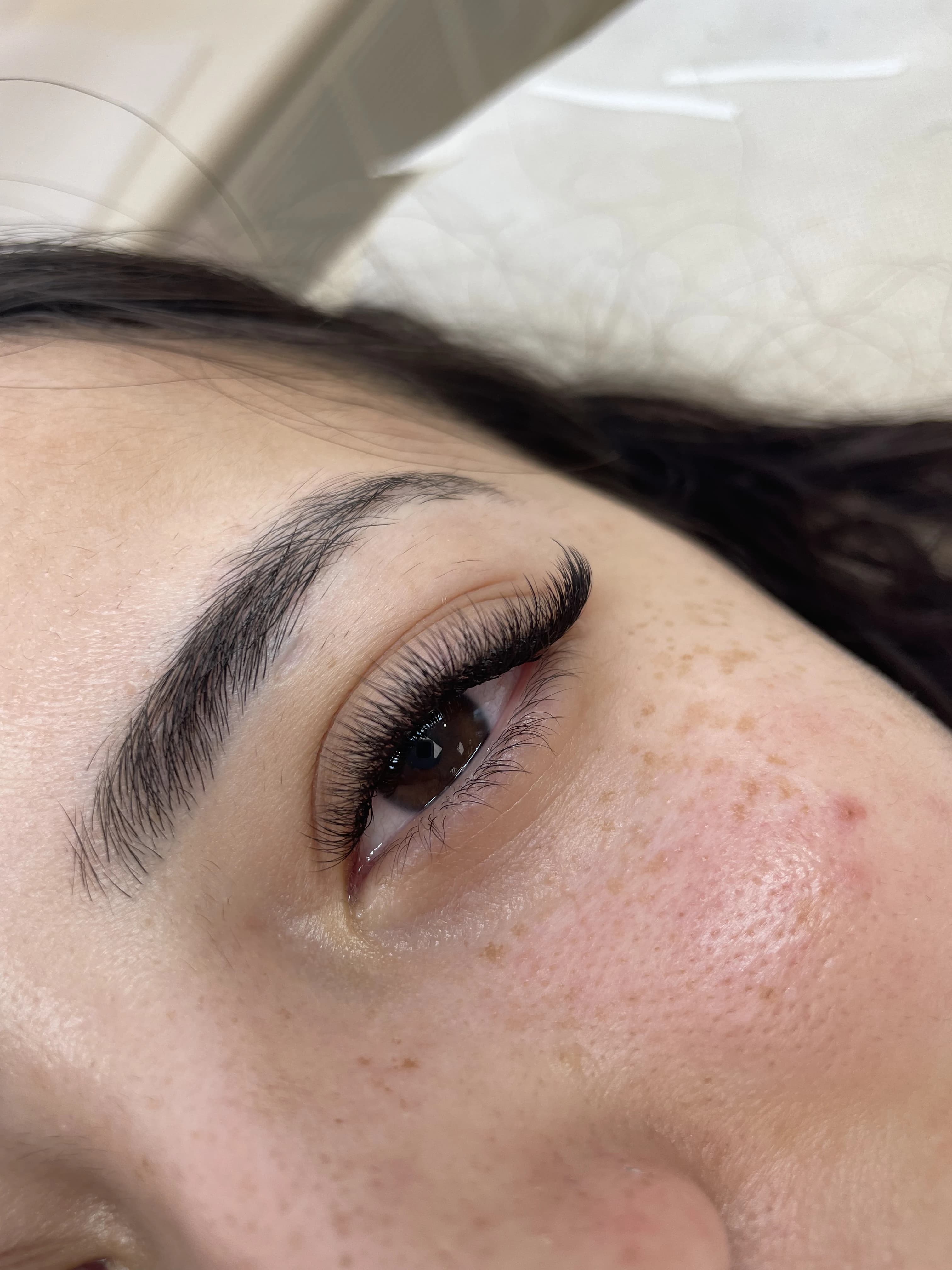 Top-down view of freckled skin with uniform 3D volume lash fringe on a salon bed at My Beauty Space Mississauga.