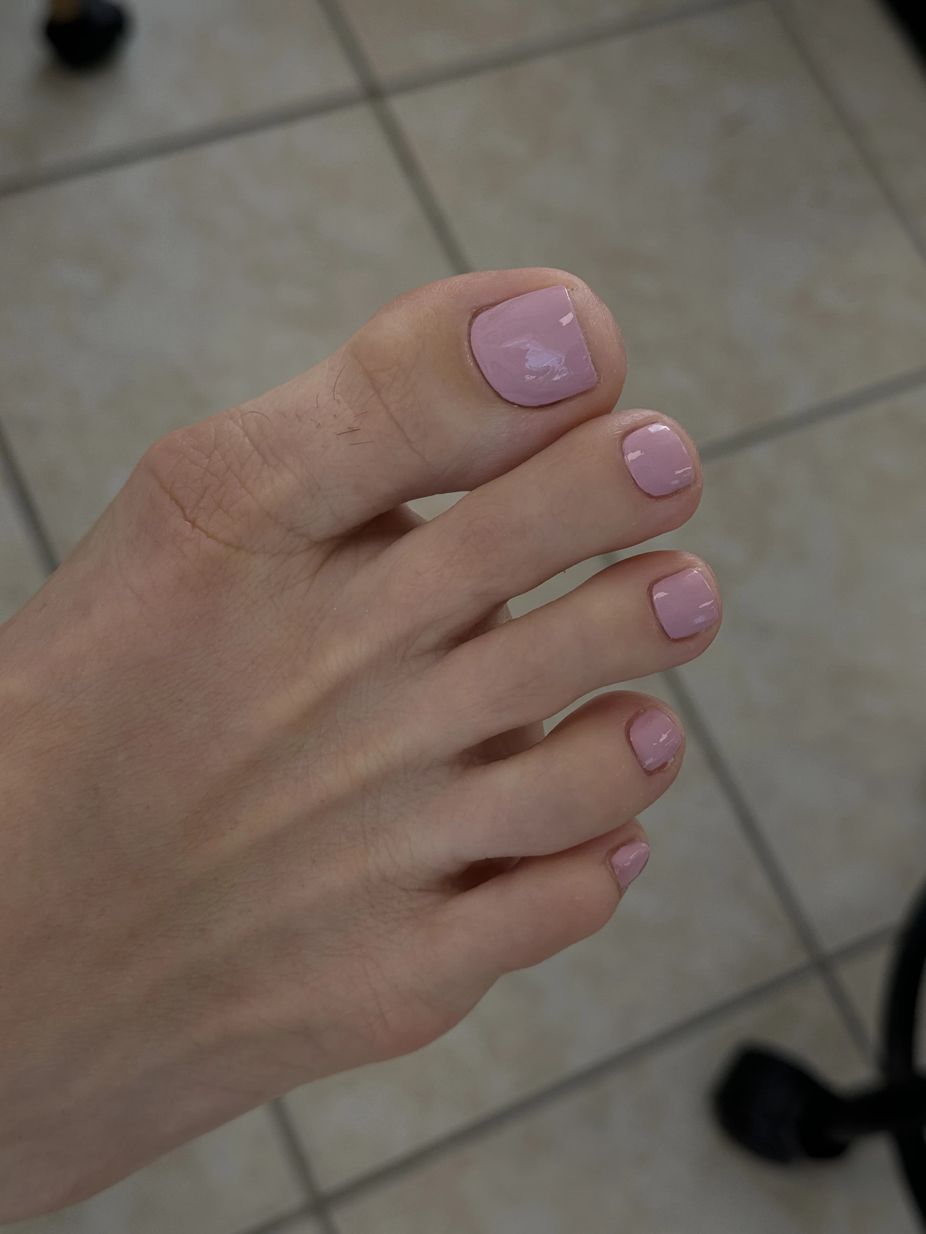 Mississauga pedicure with dusty mauve-pink regular polish on short square toes, foot angled over tiled salon flooring.