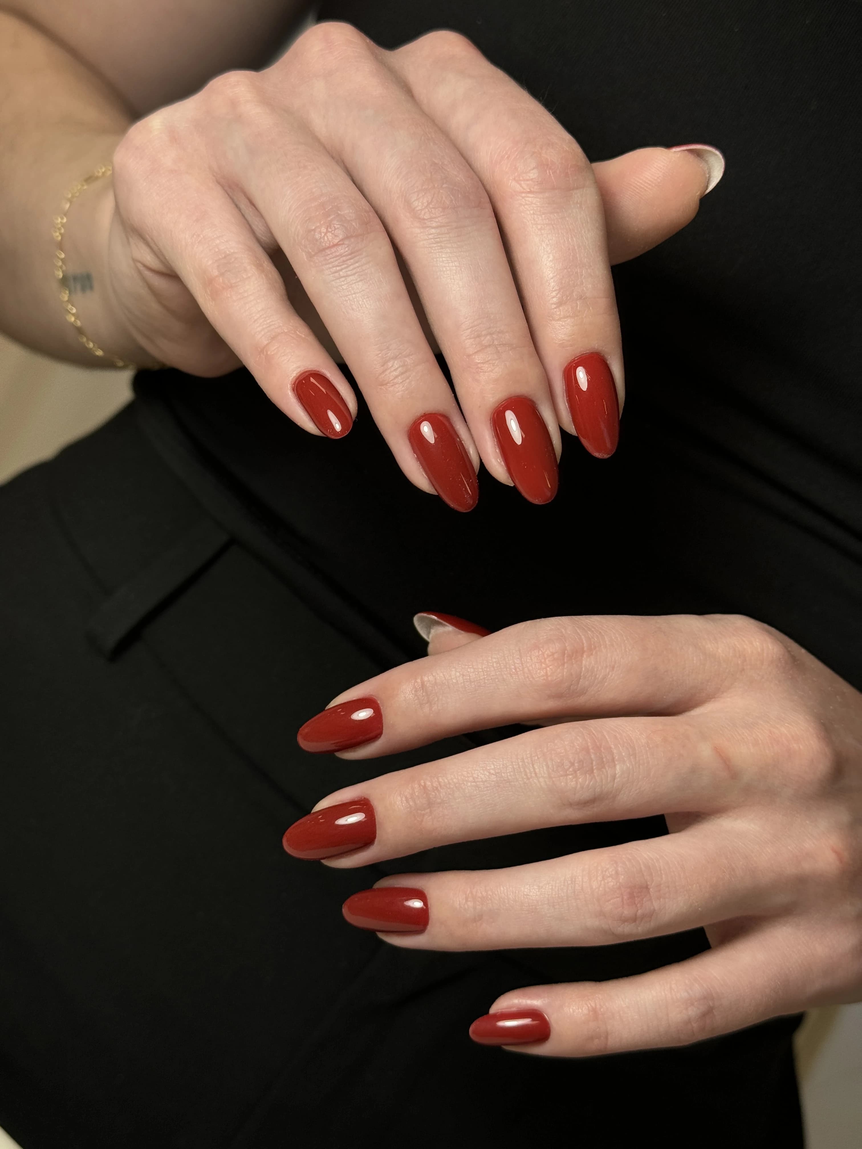 Glossy terracotta-red hard gel on almond nails with a gold chain bracelet, styled at My Beauty Space in Mississauga.