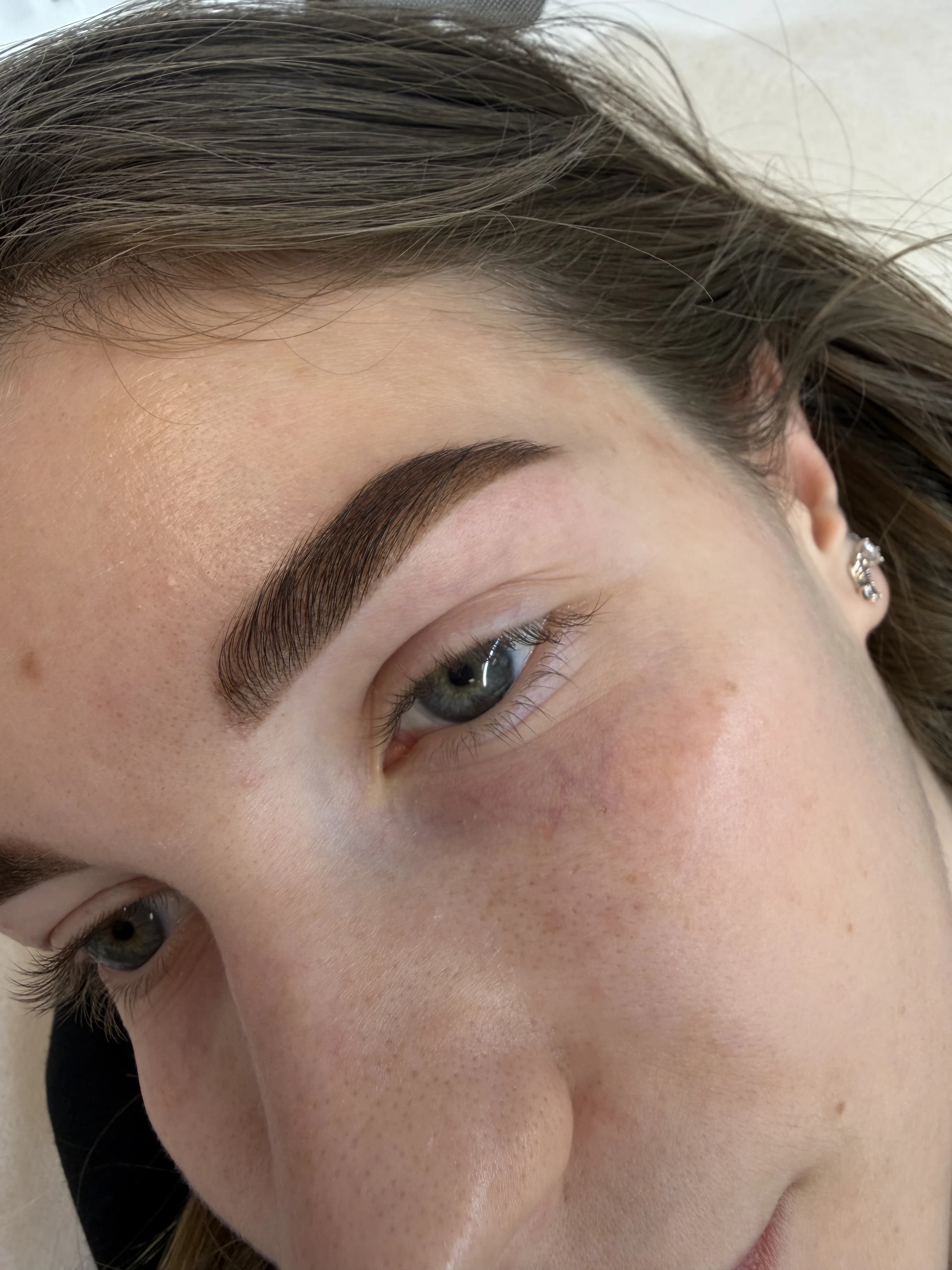 Precision-shaped dark brown brow with sharp arch and blue-grey eye, freckled skin at My Beauty Space.
