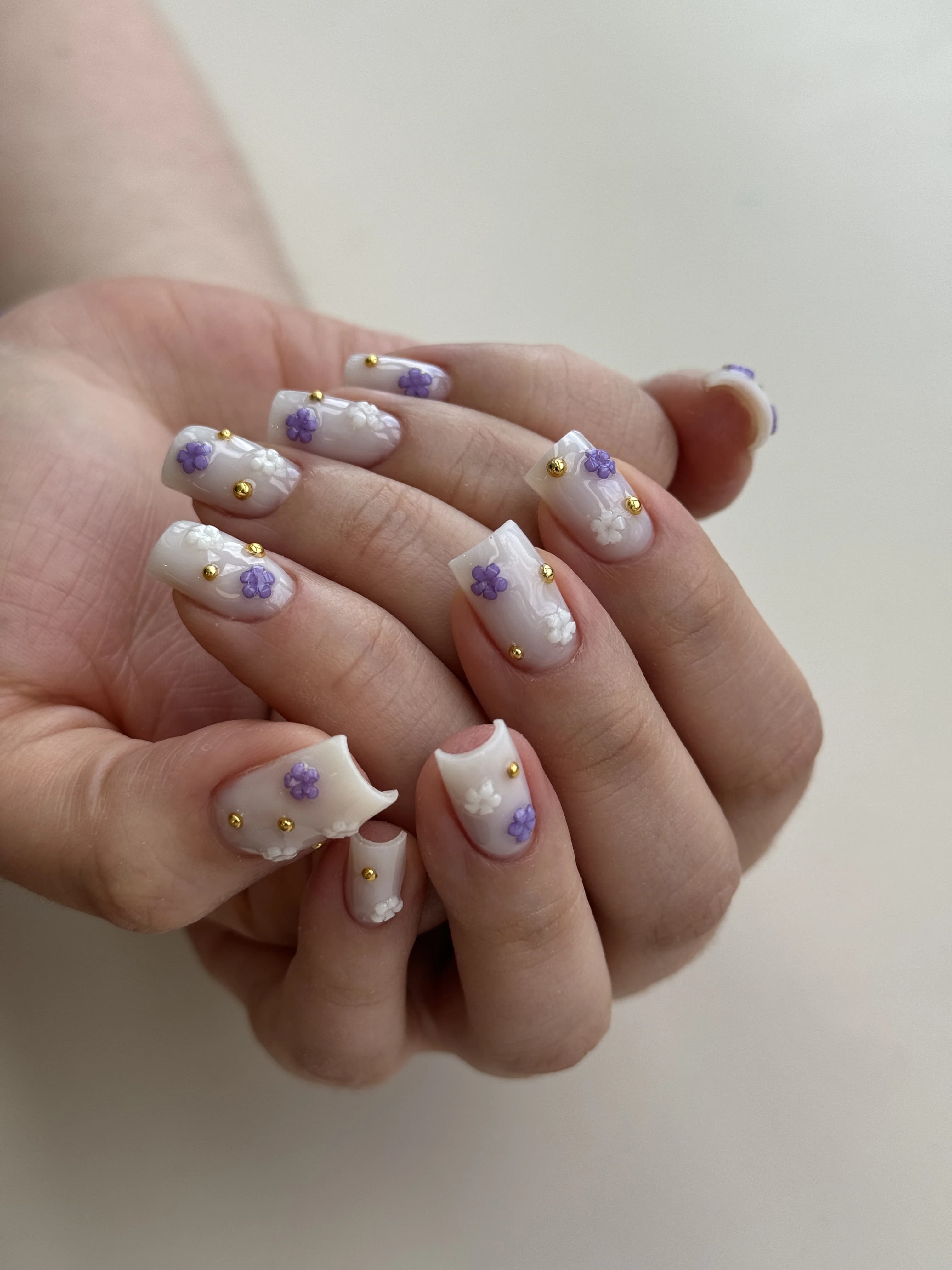 Milky marble Gel-X nail design at My Beauty Space with 3D white-purple florals and gold studs on square extensions.