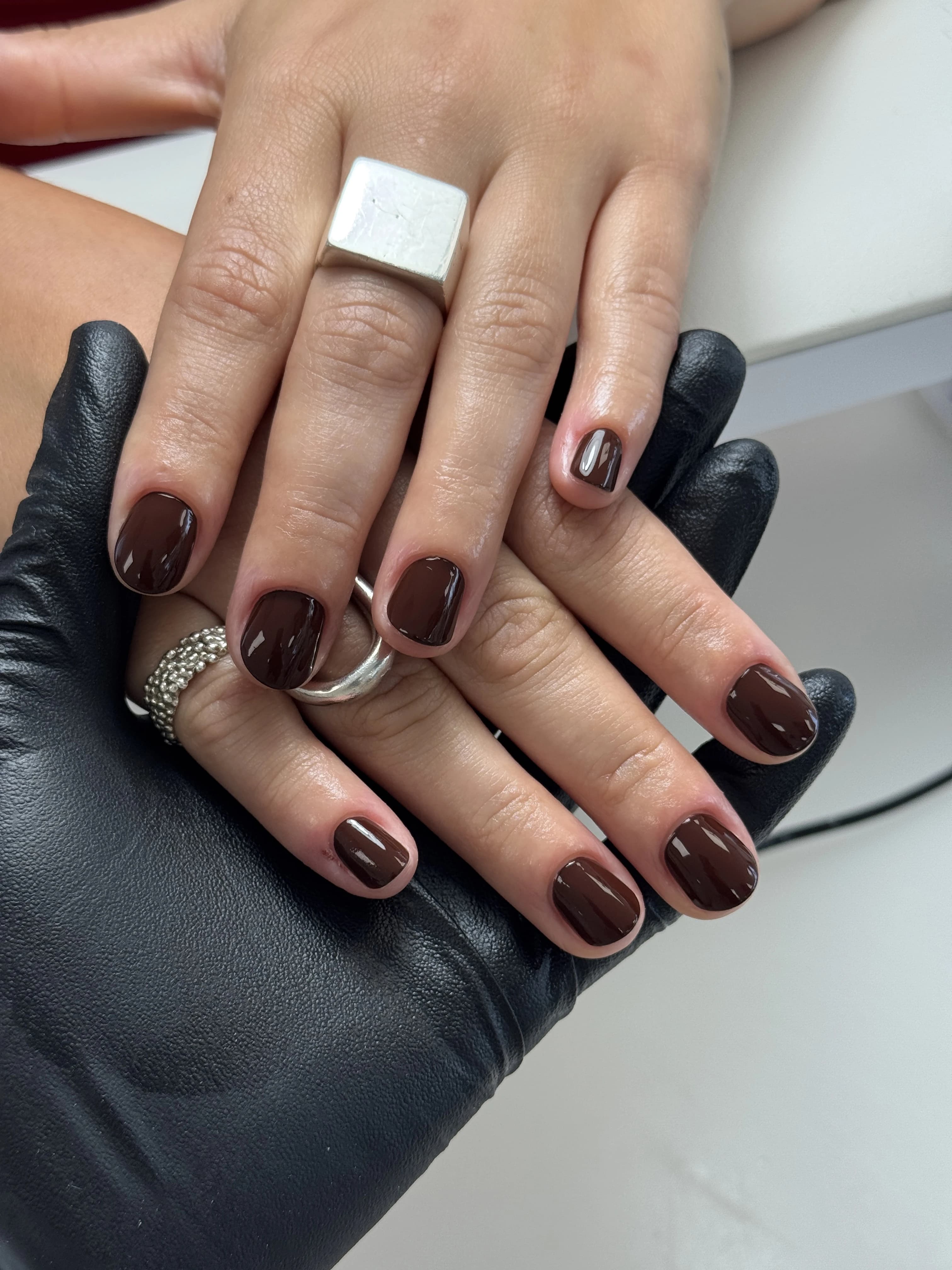 Glossy chocolate-brown regular polish on rounded-square nails with silver rings, from My Beauty Space in Mississauga.